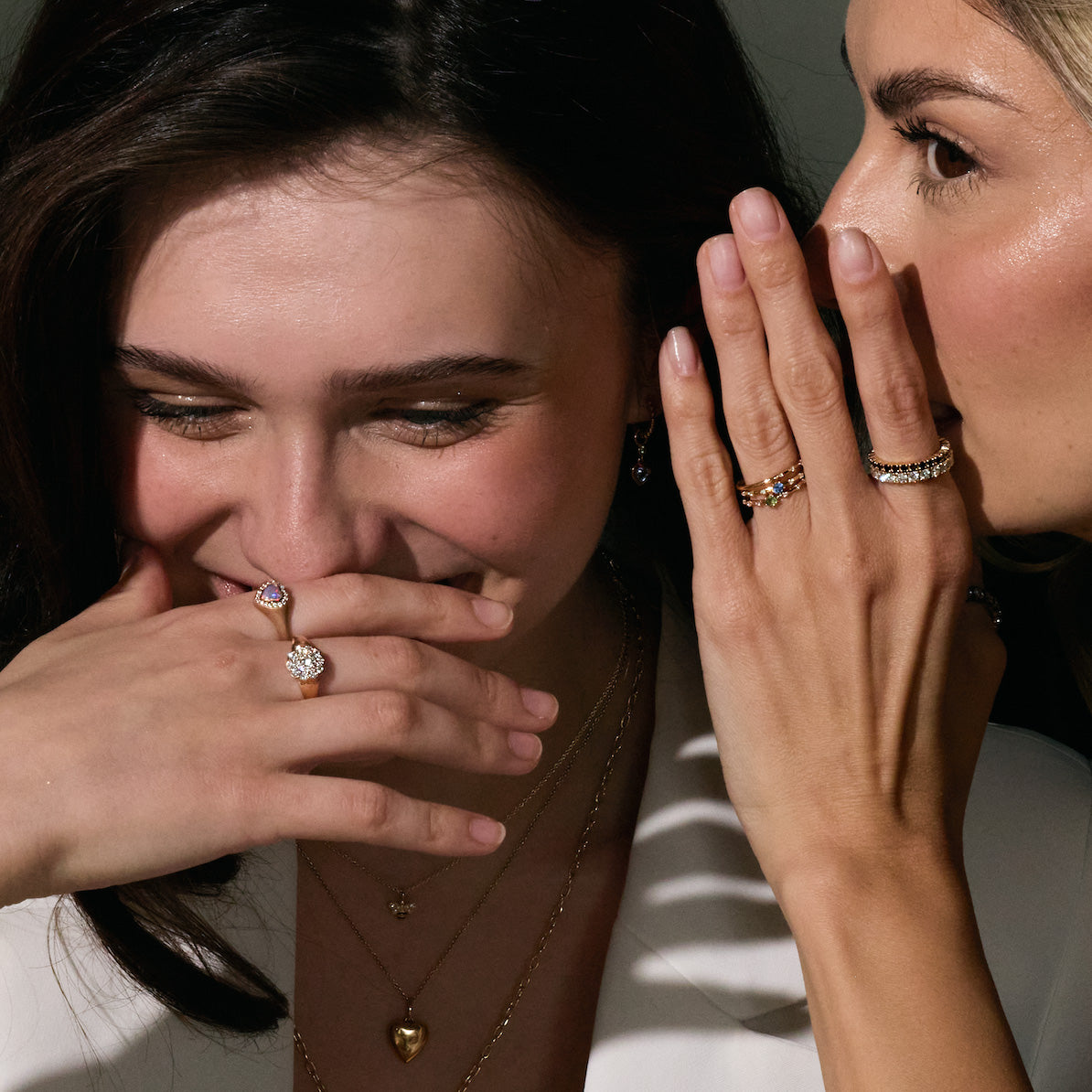 Two women whispering with a focus on their gold and precious jewelry.