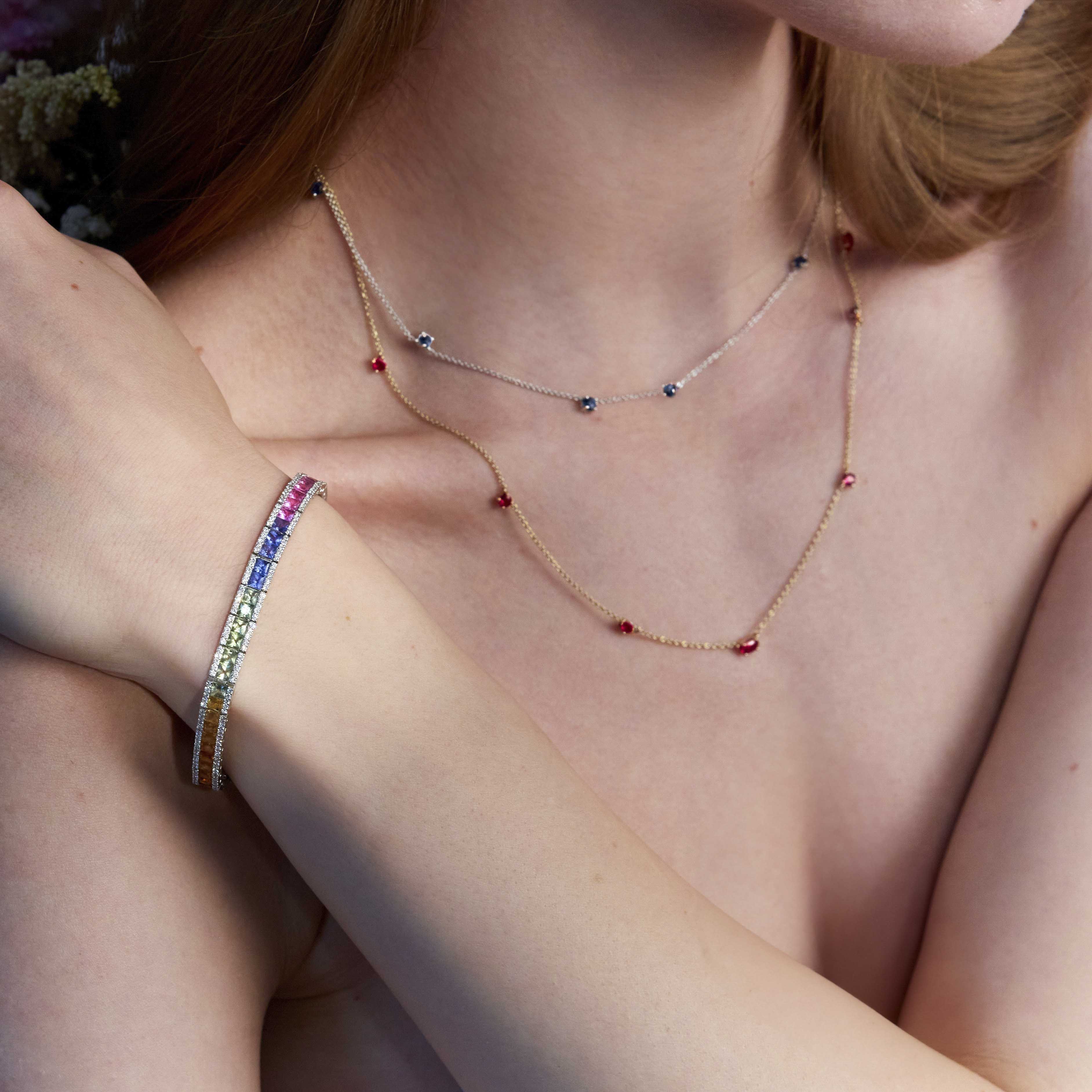 A person wearing a delicate gold chainlink necklace adorned with natural rubies and a rainbow sapphires eternity bracelet.