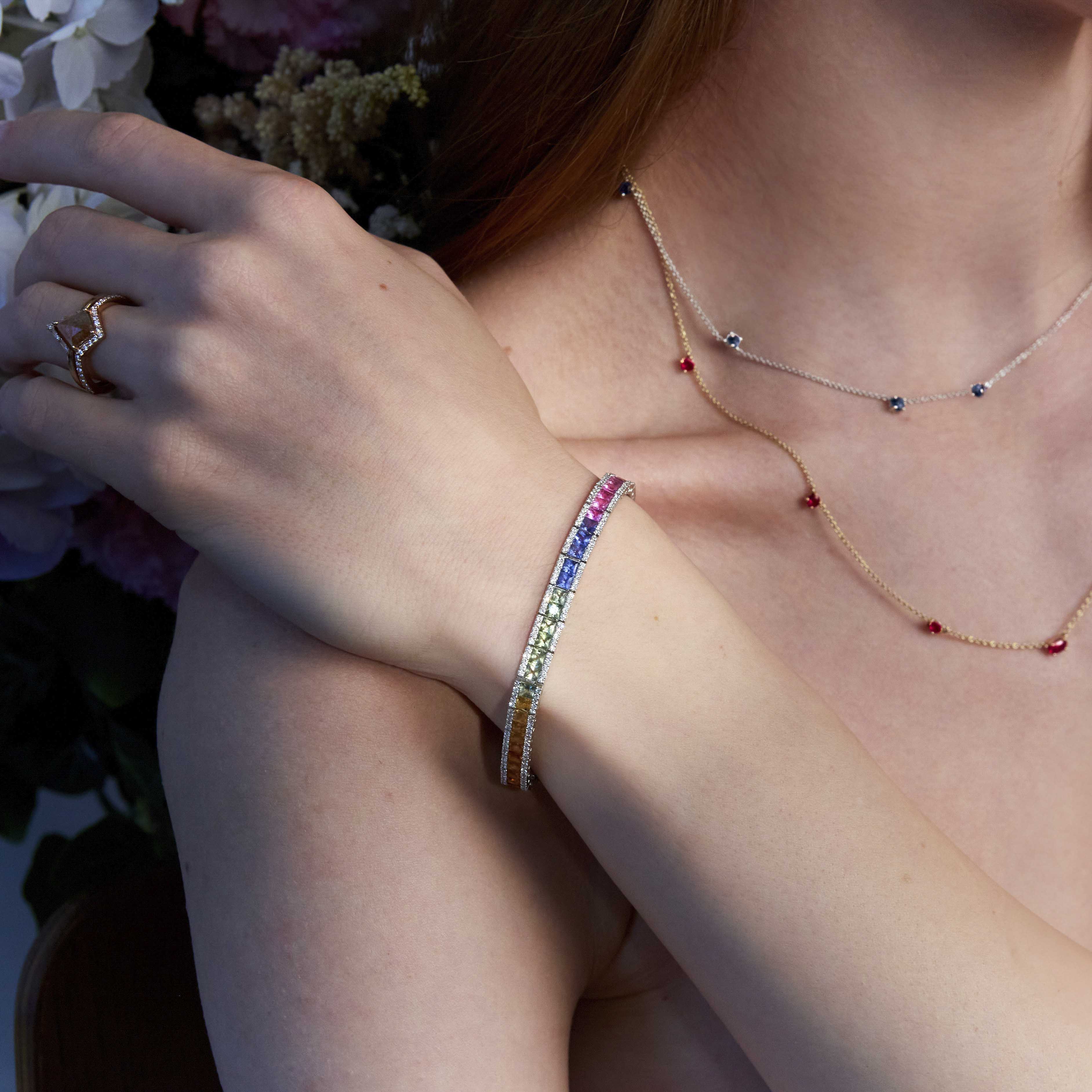 A woman wearing a tennis bracelet with rainbow sapphires and diamonds in 18k gold.