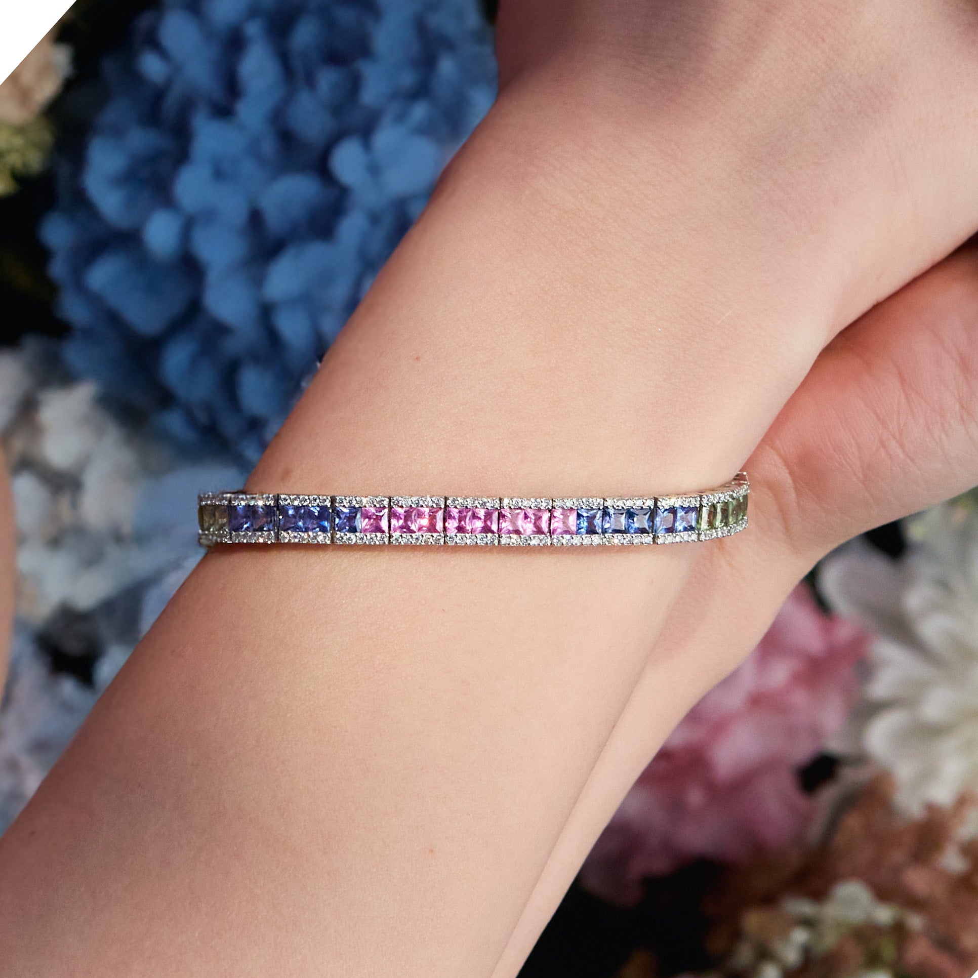 A woman wearing a tennis bracelet with rainbow sapphires and diamonds in 18k gold.