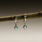 Pair of gold earrings with Australian Opals and Diamonds on a branch against a dark background.