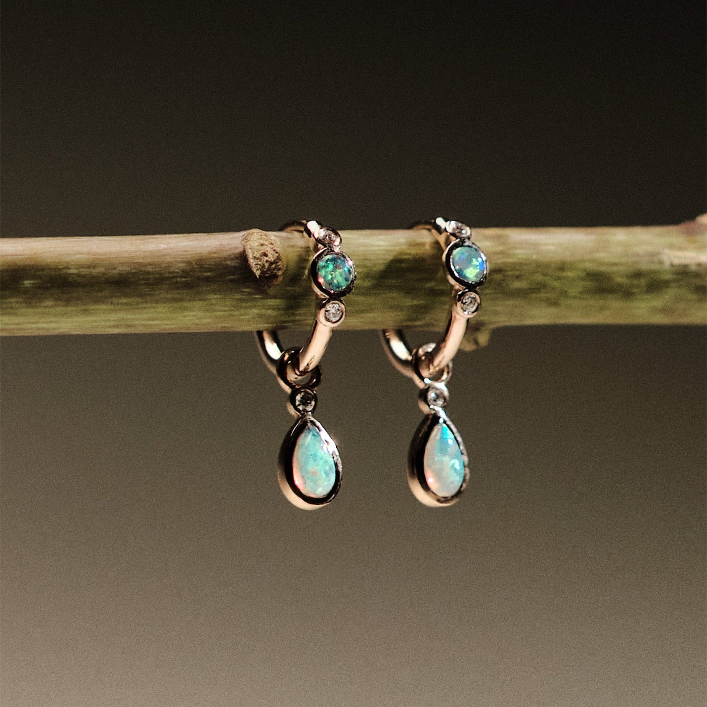 Pair of gold earrings with Australian Opals and Diamonds on a branch against a dark background.