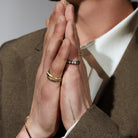 Close-up of hands with rings and a tattoo, wearing a brown suit and white shirt.