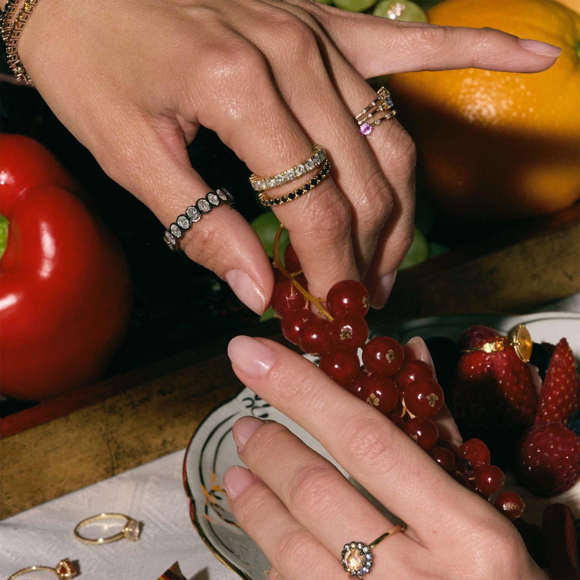 Close-up of hands with rings on a background of fruits and vegetables.
