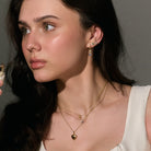 Woman wearing gold necklaces and earrings against a neutral background